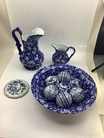 Lot showing large and small blue and white jugs, large wash basin with blue floral pattern, seven decorative balls inside basin, and small floral plate.