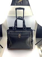 Front view of black leather rolling bag with pyramid studded trim, front lock pocket and handles