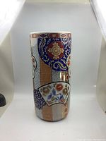 Front and side views of tall cylindrical ceramic umbrella holder with Imari style design showing detailed floral and geometric patterns.
