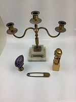 Four vintage brass decor items arranged including candelabrum, cloisonné egg, brass pin, and small figurine