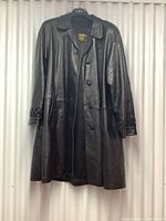 Front view of the black leather full length coat hanging showing button closure and woven detailing on cuffs