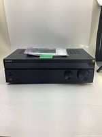 Front view of Sony vintage stereo receiver with control knobs and headphone jack, remote and manual placed on top.