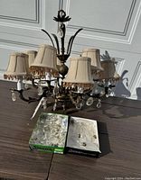 Front view of chandelier lamp with six fabric shades, metal curved arms, and crystal drops. Two boxes of clear crystal drops placed in front.