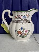Side angle showing floral pattern detail and curved handle of ceramic pitcher.