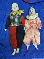 Two clown dolls placed side by side on blue background fabric, showing full bodies including attire and facial designs.