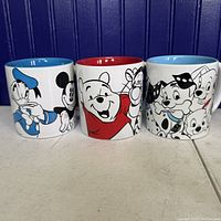 Front view of three Disney character mugs featuring Donald Duck and Mickey Mouse, Winnie the Pooh and Tigger, and the 101 Dalmatians characters with colorful interiors.