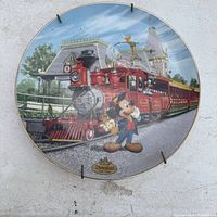 Full view of the commemorative plate showing Mickey Mouse standing in front of a red train with Disneyland park setting in the background.