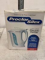Two images of the product box for a Proctor Silex Electric Kettle K2070, showing front and side views. The box highlights features such as faster than a microwave, safer than a stovetop kettle, detachable cord, automatic shutoff, boil-dry protection, and dual water windows.
