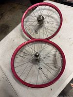 Two red bicycle rims with silver metal spokes and hubs, laid on a table surface.