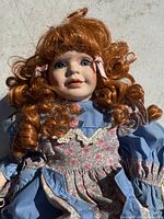 Close-up photo of porcelain doll's face showing red curly hair, blue eyes, and detailed facial features.