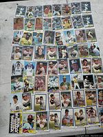 Overhead view of 58 vintage baseball cards arranged in rows on concrete surface. Cards include portraits, batting and pitching action shots from multiple teams.