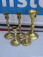 Overall view showing all five polished brass candlestick holders with round bases and taper candle cups, arranged in a row.