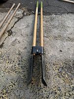 Post hole digger with two wooden handles and black metal blades laid on concrete surface