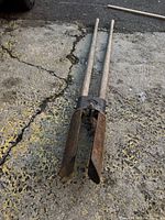 Full view of the post hole digger lying on concrete showing its full length and condition.
