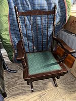 Front view of the dark wooden rocking chair with green seat cushion, showing spindle backrest and armrests.