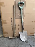 Photo of shovel and pickaxe against cardboard background, showing full length of both tools