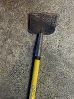 Close-up of metal scraping blade at the end of yellow handle, showing wear and use.