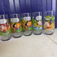 Front view of the set of 6 Camp Snoopy collectible glasses with colorful Peanuts characters in camping scenes and speech bubbles