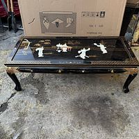 Front view of black lacquered coffee table with Asian-inspired inlay artwork and curved legs, showing overall condition and defect on the top.