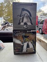 Two stacked boxes of whistling kettles showing front and back packaging and kettle design details.