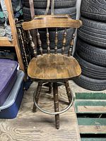 Front view of the wooden bar stool showing carved wood seat, spindle backrest, and metal footrest ring.