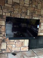 Wall-mounted Samsung flat-screen TV with black bezel above stone hearth, remote control on hearth.