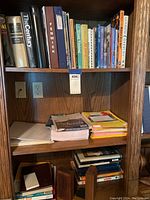Photo of bookshelf with various books, stacked papers, notebooks, and binders. Wooden bookends flank some sections.