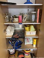Front view of cabinet shelves showing jars, towels, tools, and albums