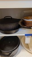 Cast iron pots and skillet on shelf, showing handles and lids
