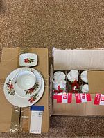 Top view of layered dishes showing dinner plate, smaller plate, teacup, and small rectangular dish with poinsettia designs and gold rims on cardboard.