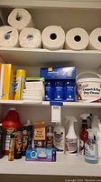 Photo of shelves with rolls of paper towels, paper products, and various cleaning liquids including Method Glass Cleaner and Carpet & Rug Dry Cleaner tub.