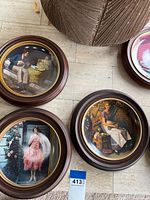 Three framed collector plates on floor including two Norman Rockwell designs and one Donald Putman Women of the West plate, with beige tile flooring and partial furniture