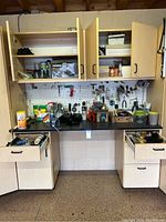 Photo of the tool bench countertop with cabinets above, showing various small tools and bottles with two drawers partly open.
