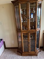 Full front view of vintage burlwood curio cabinet with glass doors and shelves, some decorative figurines inside but noted as not included in sale.
