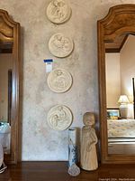 Four alabaster Madonna wall plates mounted vertically on wall, with little girl statue standing beside a ceramic vase and jewelry jar