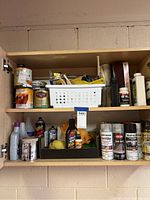Wooden shelf with assorted cans, bottles, cleaning products, and tools showing a variety of weathered DIY supplies stored in a garage.