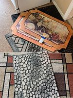 Photo showing eight stacked doormats with visible designs: vintage wine and grape theme, stone texture, geometric pattern, and ornate black rubber mat.