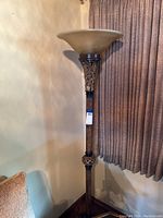 Full view of the decorative tall floor lamp with beige glass shade and wooden pole in corner near curtains.