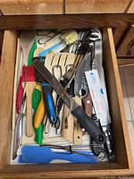 Top view of assorted kitchen utensils showing various spatulas, wooden spoons, knives, whisks, scissors and basting brushes in a wooden drawer.