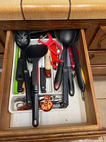 Drawer open showing a variety of kitchen utensils in plastic tray organizer