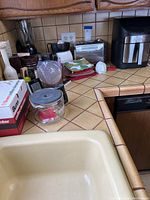 Kitchen counter with various small appliances and kitchenware including a Braun mixer still in box, glass containers, and oven mitts.