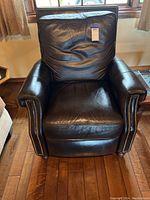 Front view of black leather reclining armchair with studded armrests, showing cushioned seat and backrest.