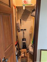 Closet interior showing step ladder, brooms, brushes, and cleaning items inside.