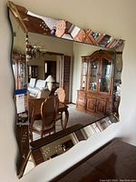 Frontal view of the decorative wall mirror mounted on a wall reflecting furniture and chandelier in a room.
