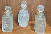 Photo showing the set of three etched glass decanters with faceted glass stoppers on wooden surface.