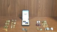 Photo showing 14 assorted cufflinks laid out on a wooden surface, including a pair in a blue and white branded box.