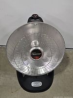 Front view of Presto HeatDish parabolic electric heater showing the silver reflector dish, central heater element, and black base with control knob.