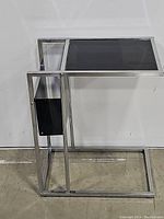 Side view of the black glass top and chrome metal frame of the modern C-shaped side table, showing its structure and condition.