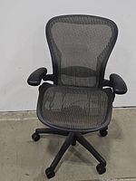 Front view of black mesh office chair showing mesh seat and back, with armrests and wheeled base.
