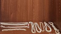 Eight strands of white pearl necklaces laid out on a wooden surface, showing different lengths and clasp types.